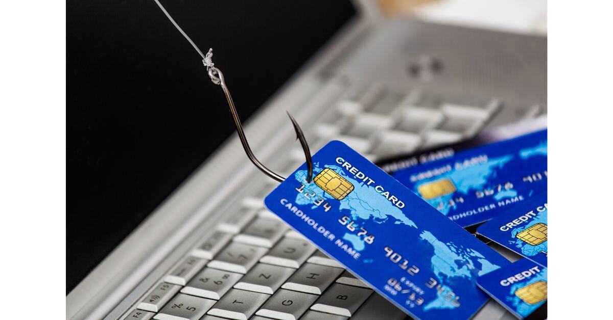 Image of a keyboard with a fishing hook through one of several blue chip and pin credit cards with a paler blue world map on them.  All visually representing a phishing scam