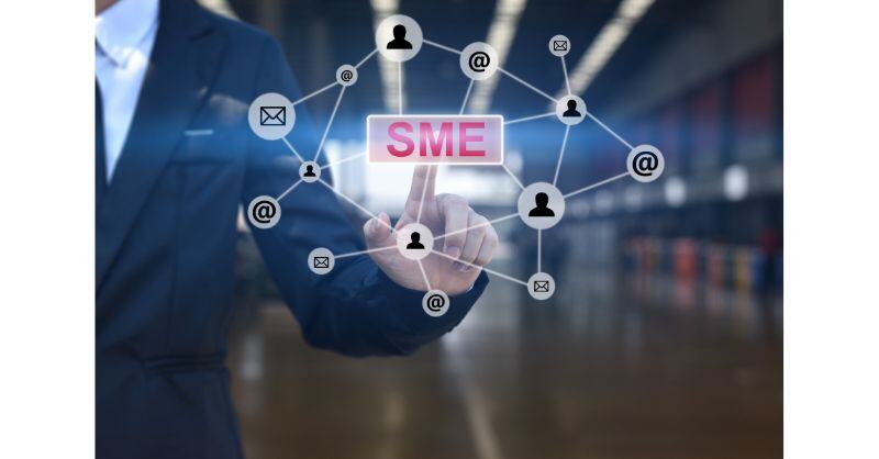 Five Key IT Trends UK SMEs Need to Watch in 2025.  A man in a suit points to a screen - we're on the other side of that screen.  He's mapping out with his fingers lines between different IT icon's and symbols - connecting the trends for SME's.  The word SME is in the middle of the image in pink.