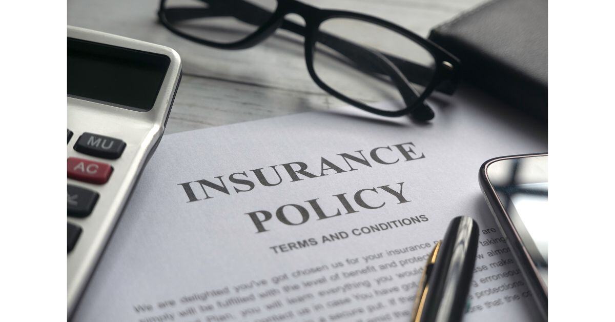 Close-up of a printed document headed 'Insurance Policy' with an expensive pen, glasses and a calculator next to it.  To accompany the blog, 